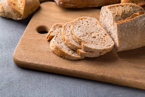 Freshly baked sliced bread on wooden cutting board on the grey stone table, macro - Фото, зображення
