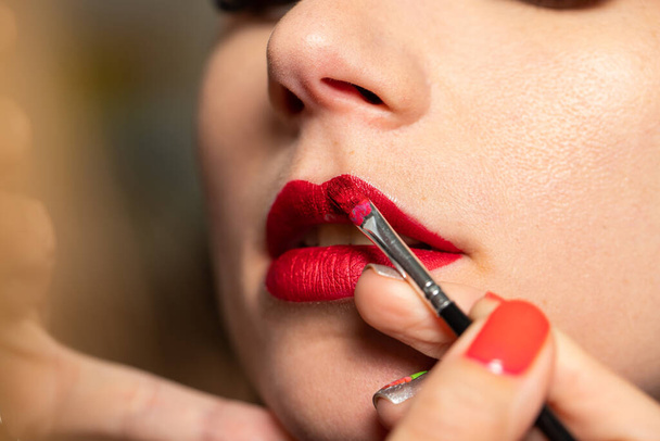 Ο μακιγιέρ ζωγραφίζει τα χείλη στον πελάτη με κόκκινο κραγιόν - Φωτογραφία, εικόνα