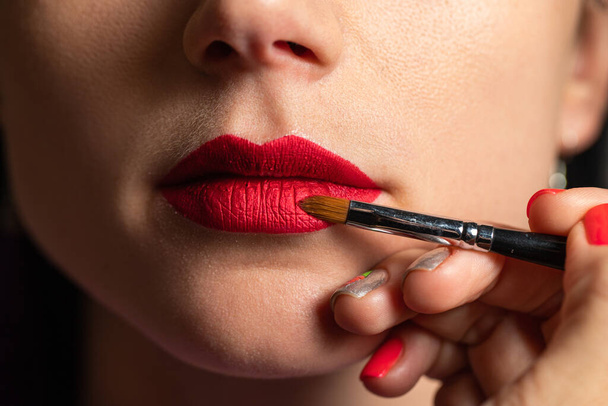 Meikkitaiteilija maalaa huulet asiakkaalle punaisella huulipunalla
 - Valokuva, kuva