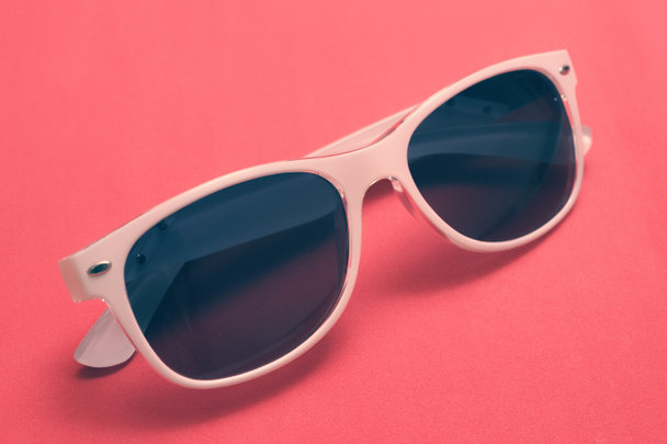 Retro-Sonnenbrille mit weißem Rahmen und dunkler Linse auf rosa Hintergrund - Foto, Bild