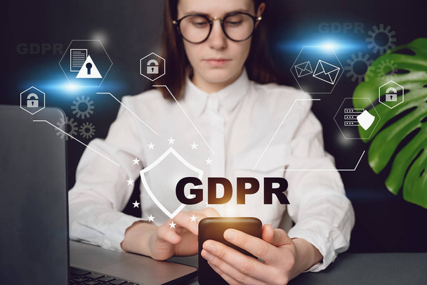 Close up front view young woman holding smartphone, with text GDPR. Data Protection Regulation, sitting at desk near pc. Cyber security and privacy. Protection of private personal data. - Photo, Image
