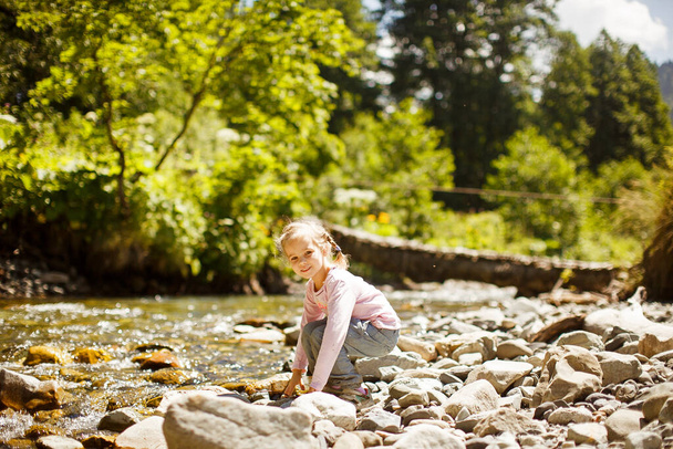 small girl sit on rocks shore of mountain river  - Photo, Image