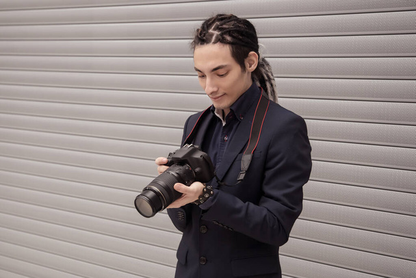 A handsome young guy, a photographer, looks at the camera, takes aim, takes pictures. Shoot, snapshot. A man with dreadlocks. See the pictures taken. Copy space. - Foto, immagini