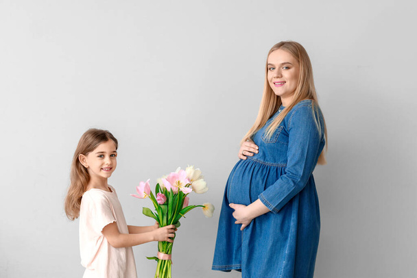 Niña saludando a su madre embarazada con flores sobre fondo claro
 - Foto, Imagen
