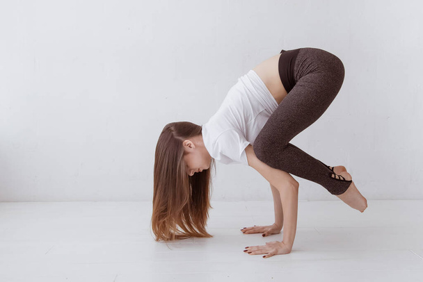 Beautiful young woman at home on a white background engaged in yoga, standing in a pose Crane (Crow) Pose, Bakasana (Kakasana), full length. Lifestyle. - Foto, Bild