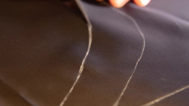 Портной вырезает линии на ацетатной ткани шелковой подкладки с его мелом, чтобы сделать костюм
 - Кадры, видео