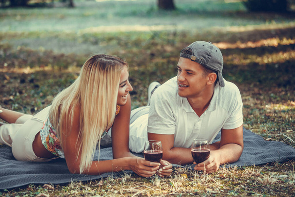 Hermosa pareja joven hablando, coqueteando y disfrutando de una copa de vino en un romántico picnic en un parque
 - Foto, imagen