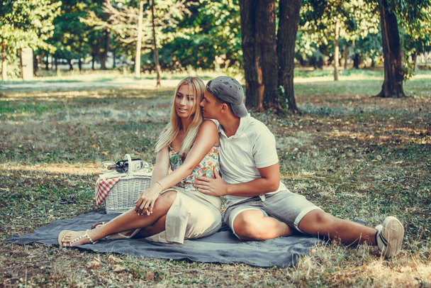 Όμορφο ζευγάρι αγάπη αγκαλιάζει και φιλιά, ενώ απολαμβάνετε στο γρασίδι στο πάρκο  - Φωτογραφία, εικόνα