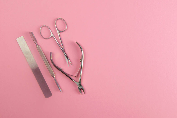 Manicure schaar, zaag en spijkerzak evenals nagelriemen snijders staan op een roze achtergrond. Top uitzicht met duidelijke ruimte - Foto, afbeelding