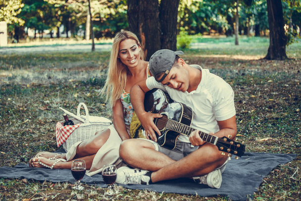 Mladý pár se baví, mají romantický piknik v parku. Hraní na kytaru a zpěv. Romantika, randění a milostný koncept.  - Fotografie, Obrázek