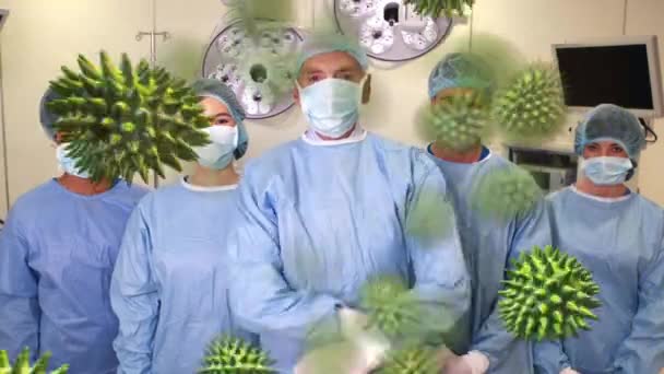 Animace makrokoronárních buněk Covid-19, které se šíří po mužských a ženských lékařech v ochranných oděvech a obličejové masce, stojící na chirurgickém sále a dívající se na kameru v pozadí. - Záběry, video