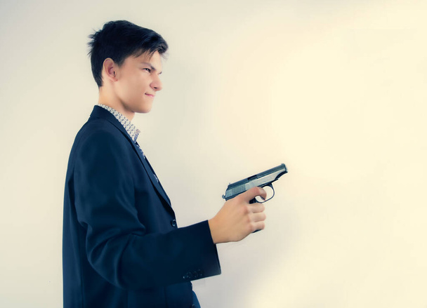 Profile view of a young man wearing a business attire holding a gun up in front of him. Isolated on cthjv, copy space - Photo, image