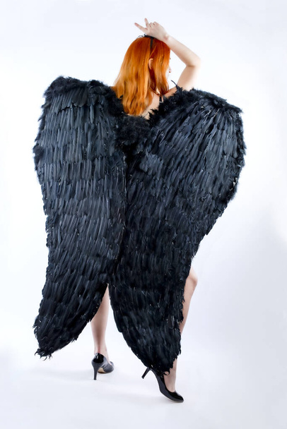 Rear view on the woman in black lingerie with angel wings on a gray background. Isolated. Fallen Angel - Φωτογραφία, εικόνα