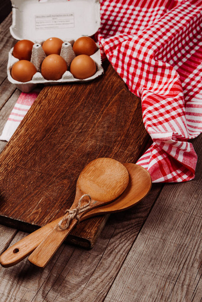Ξύλινη επιφάνεια κοπής σε ξύλινο φόντο με σκόρδο, κουτάλες και αυγά - Φωτογραφία, εικόνα