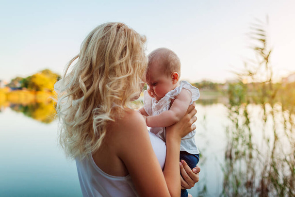 Mothers day. Young woman holding and kissing baby girl by spring river. Family walking spending time together outdoors. Kid exploring world - Fotoğraf, Görsel