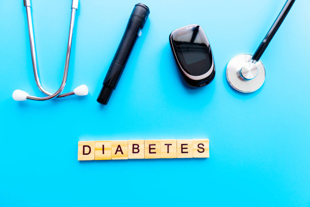 Diabetes Wooden Text. Medicine, Diabetes, Glycemia, Health care and people concept - close up of lancelet, Glucose meter and stethoscope on blue background. - Photo, Image