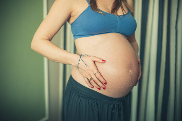 Eine schwangere Frau in Trainingskleidung berührt ihren Bauch - Foto, Bild