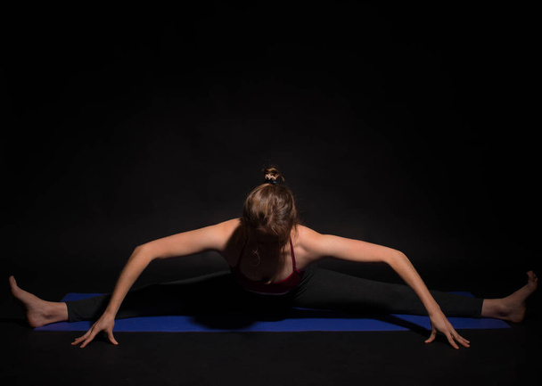młody sport kobieta robi jogę na macie na ciemnym tle - Zdjęcie, obraz