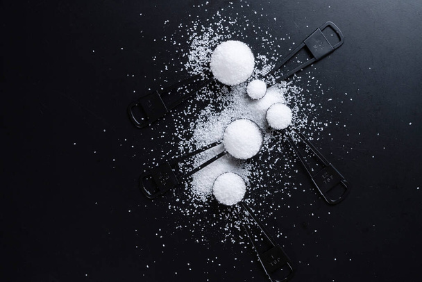 Black measuring spoons with salt on black background. - Foto, immagini