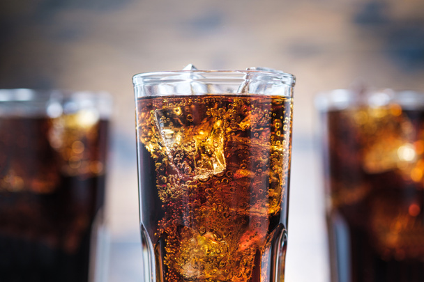 Closeup cola with bubbles and ice cubes. Cold fizzy drink on wooden background - Photo, Image
