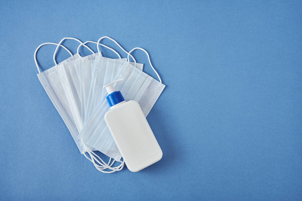 White antiseptic bottle with dispenser lying on medicine masks on blue background, top view - Zdjęcie, obraz