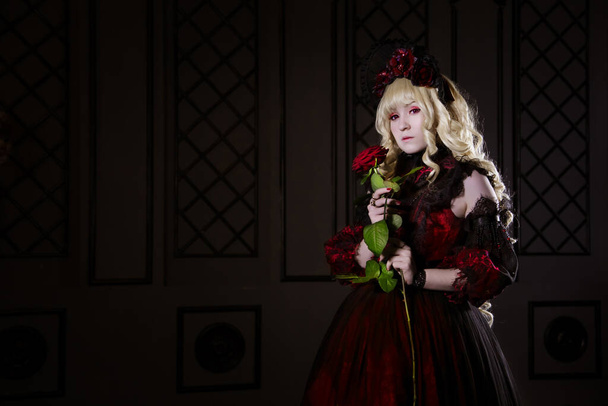 A beautiful, small, blond girl, holding a rose in her hands, in a red lush old dress. The woman is the vampire Claudia. japanese style lolita, cosplay cute. Street fashion. - Fotoğraf, Görsel