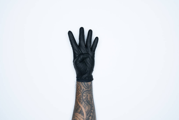 Siyah lastik eldivenli bir adamın eli ve hareketleri beyaz arka planda izole edilmiş dört işaret gösteriyor.. - Fotoğraf, Görsel