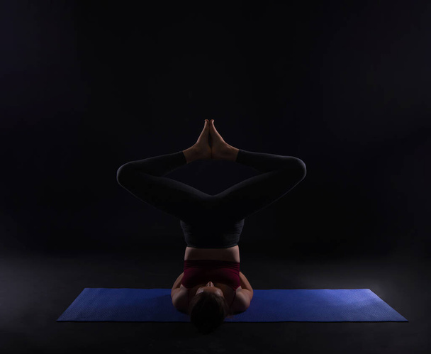 fiatal sport nő csinál jóga a szőnyegen felett sötét háttér - Fotó, kép
