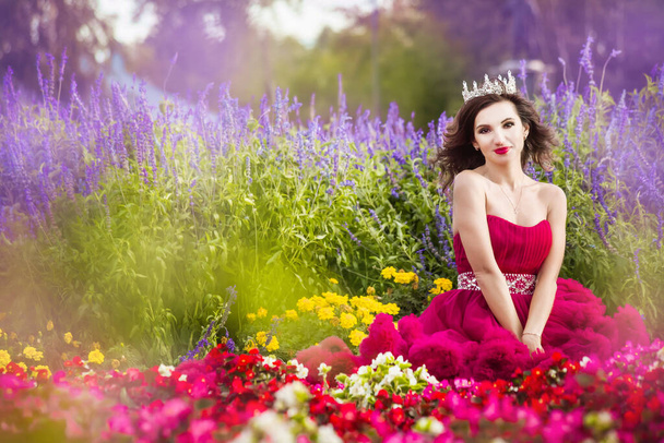 A beautiful woman, a princess in a red dress, sits by in a blooming garden. Medieval fantasy, American - Fotoğraf, Görsel