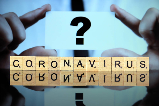 WROCLAW, POLAND - MARCH 30, 2020: The word CORONAVIRUS made of wooden letters, and man holding a business card with question mark in the background. Coronavirus (COVID-19) global disease 2020. - Foto, Imagem