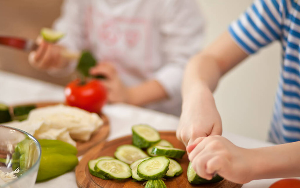 Happy children prepares vegetables for salad in home kitchen. Healthy eating - Foto, afbeelding