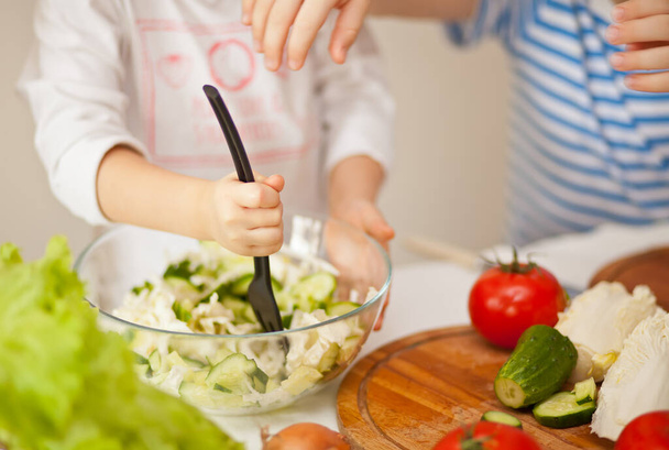 Happy children prepares vegetables for salad in home kitchen. Healthy eating - Photo, Image