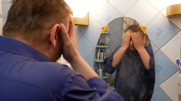 man kijkt naar zichzelf in de badkamer spiegel - Video