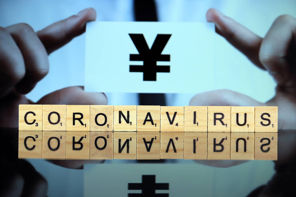 WROCLAW, POLOGNE - 30 MARS 2020 : Le mot CORONAVIRUS fait de lettres en bois, et l'homme tenant une carte de visite avec le signe yen ou yuan en arrière-plan. Coronavirus (COVID-19) maladie mondiale 2020
. - Photo, image