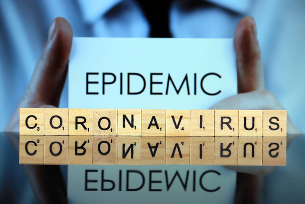 WROCLAW, POLAND - MARCH 30, 2020: The word CORONAVIRUS made of wooden letters, and man holding a business card with the word EPIDEMIC in the background. Coronavirus (COVID-19) global disease 2020. - Photo, Image