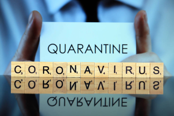WROCLAW, POLAND - MARCH 30, 2020: The word CORONAVIRUS made of wooden letters, and man holding a business card with the word QUARANTINE in the background. Coronavirus (COVID-19) global disease 2020. - Foto, Imagem