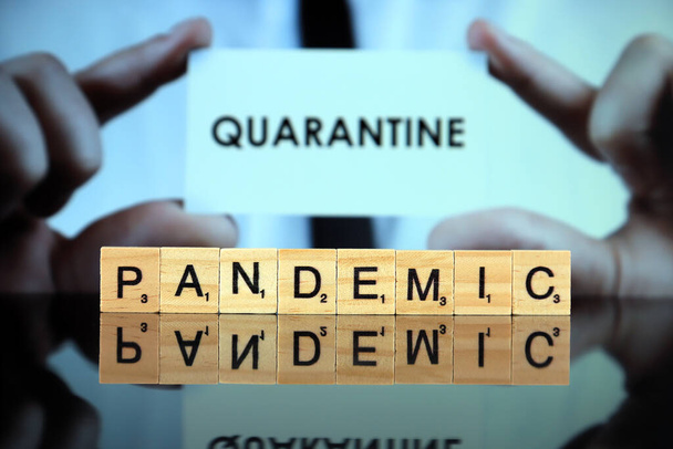 WROCLAW, POLAND - MARCH 30, 2020: The word PANDEMIC made of wooden letters, and man holding a business card with the word QUARANTINE in the background. Coronavirus (COVID-19) global disease 2020. - Foto, imagen