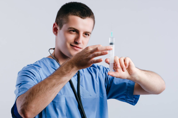 Portrait of serious young doctor intern holding syringe for injection isolated on white background - Foto, Imagen