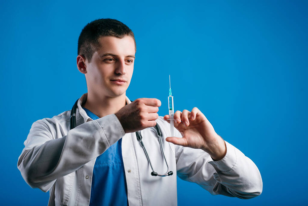 Porträt eines fokussierten männlichen Arztes mit Spritze, der bereit ist, Patienten isoliert auf blauem Hintergrund zu behandeln - Foto, Bild