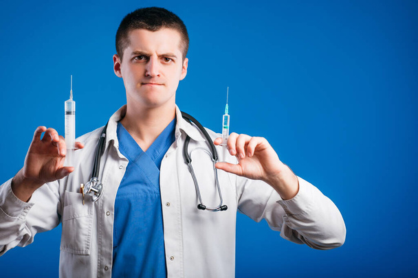Portrait of funny emotional male doctor with two syringes isolated on blue background - Photo, image