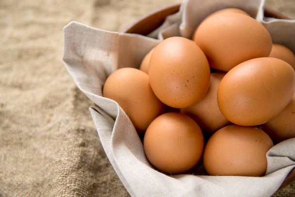 Куриные яйца в тарелке с льняной салфеткой на деревянном фоне с мешковиной. Природные продукты
. - Фото, изображение