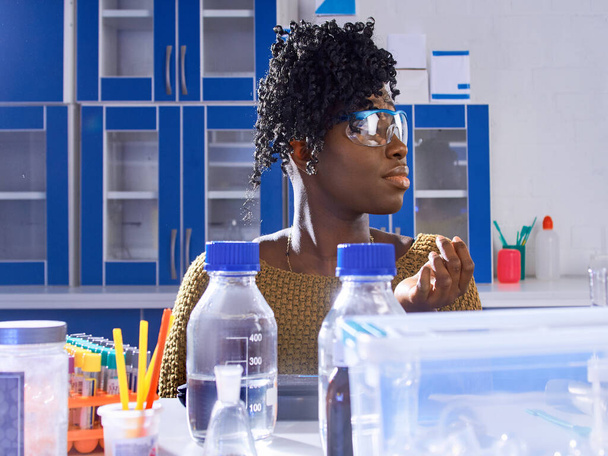 Genç Afrikalı kadın teknisyen ya da koruyucu gözlüklü bilim adamı modern araştırma laboratuvarında biyolojik veya tıbbi sıvı örnekleriyle çalışıyor.. - Fotoğraf, Görsel