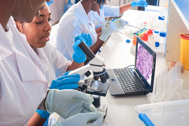 La tecnología femenina africana, la bata blanca de los científicos y los guantes hacen la prueba del pcr, trabajan con el microscopio en el laboratorio moderno o la instalación de investigación. Análisis de tejido pulmonar de pacientes con COVID-19, casos clínicos. - Foto, Imagen