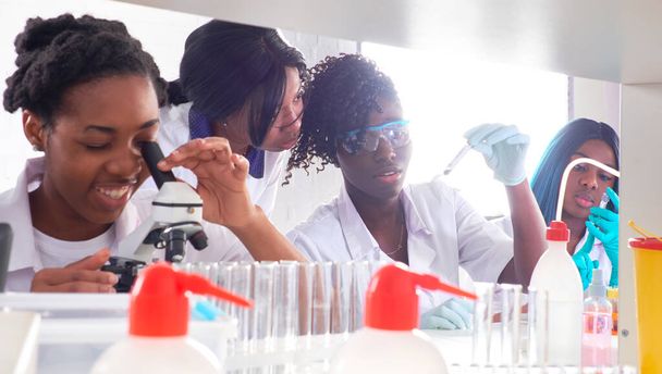 Testfaciliteit. Jonge Afrikaanse vrouwelijke wetenschappers of geneeskundestudenten, positieve energieke vrouwen, werken samen bij het uitvoeren van bloed-, nucleïnezuur- en andere medische tests op monsters van Covid-19 patiënten. - Foto, afbeelding