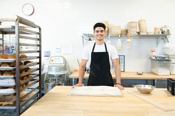 Charmant homme hispanique portant un tablier et travaillant dans une boulangerie avec un sourire
 - Photo, image
