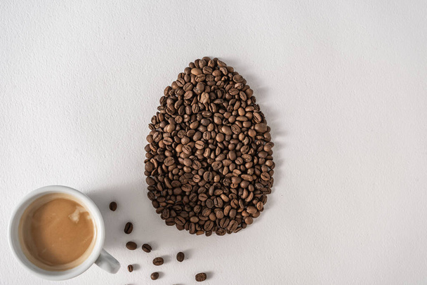 Creative flat lay composition with easter egg shape made of coffee roasted beans.Pastel colors and soft shadows. Realistic aesthetic look. Contemporary style. - Photo, Image