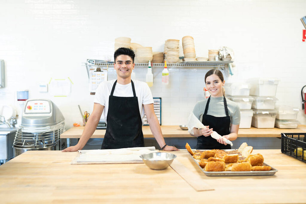Портрет команды пекарей, работающих над выпечкой и хлебом на кухонном столе и улыбающихся
 - Фото, изображение