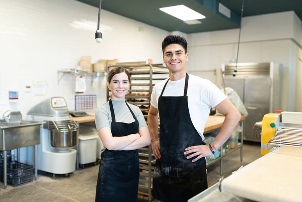 Portrait de deux jeunes boulangers travaillant en équipe dans une cuisine de boulangerie et souriant
 - Photo, image