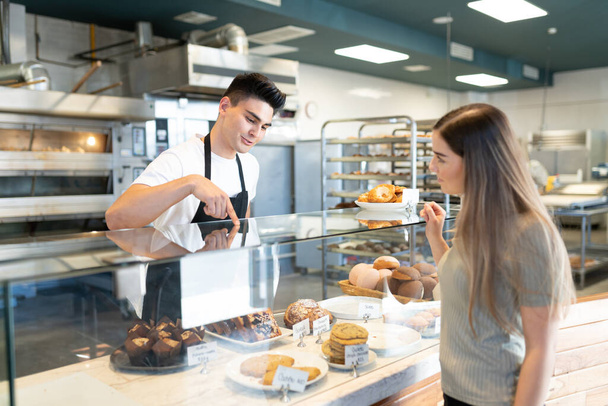 Un panadero guapo recomendando pasteles y pan a un cliente en una panadería.
 - Foto, imagen