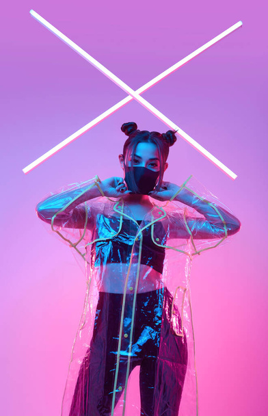 Retrato de hermosa máscara de virus Mujer asiática que usa protección facial y impermeable alrededor de luces ultravioletas de neón brillantes de colores posando en el estudio
 - Foto, imagen